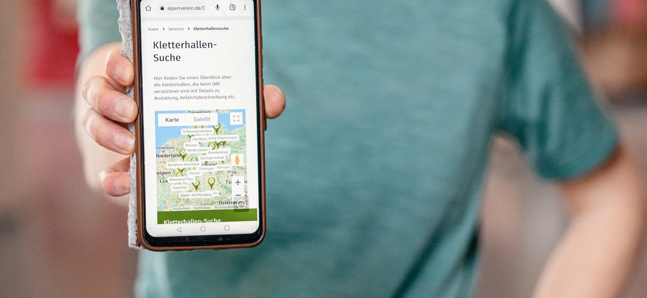 Eine Frau hält ihr Smartphone in die Kamera - auf dem Display sieht man die Kletterhallensuche | © DAV/Marisa Koch