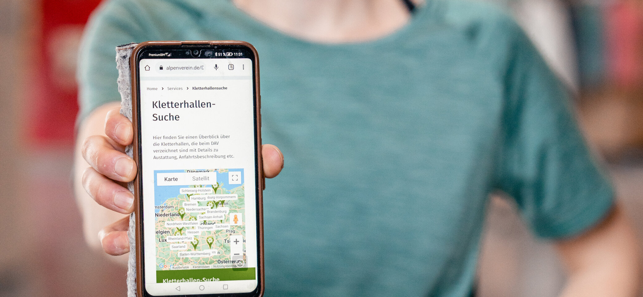 Eine Frau hält ihr Smartphone in die Kamera - auf dem Display sieht man die Kletterhallensuche | © DAV/Marisa Koch